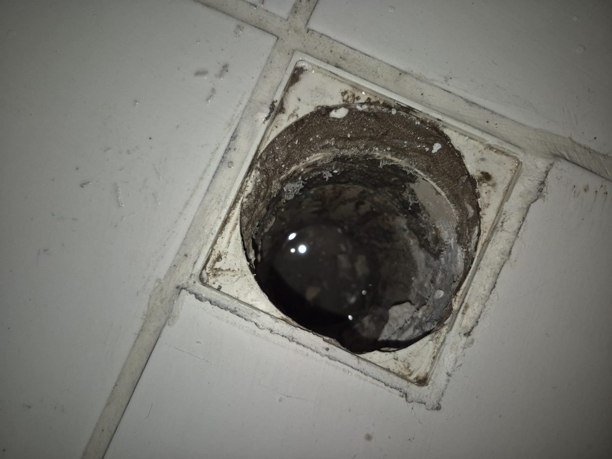 Ralo aberto no piso com entulho de obra e água parada dentro