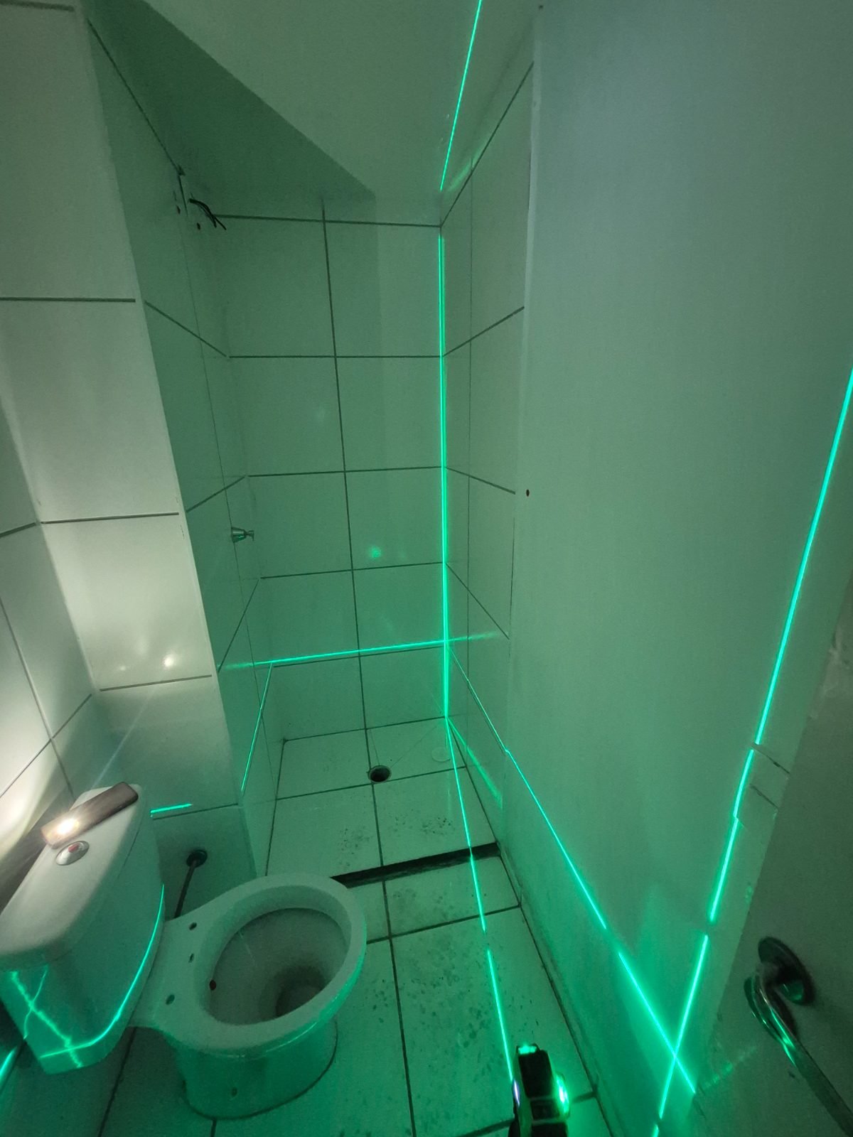 Nível a laser projetando linhas verdes nas paredes de um banheiro